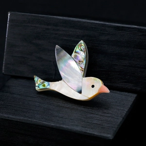 Vue macro d'une broche oiseau avec des ailes en nacre d'abalone et corps en nacre blanche