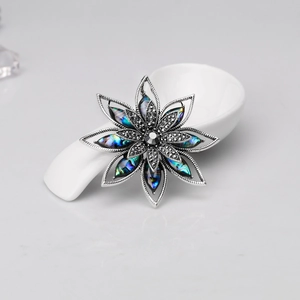 Dettaglio di una spilla a fiore vintage con petali in madreperla e cristalli grigi incastonati