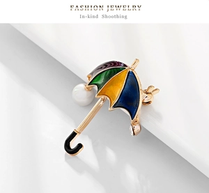 Detailed macro view of gold-plated umbrella brooch with enamel and a white pearl drop