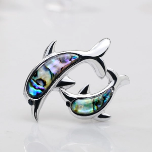 Macro view of double dolphin brooch featuring iridescent abalone shell inlay on silver metal
