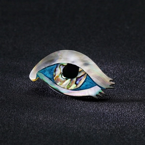 Primo piano della spilla a forma di occhio in abalone naturale iridescente su fondo nero