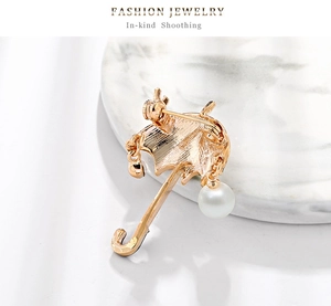 Detail of golden umbrella brooch with hanging pearl and secure pin clasp on back