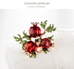 Macro detail of a vintage pomegranate brooch with red glaze fruits and green enamel leaves