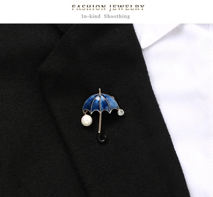 Detail of umbrella brooch with blue enamel and pearl pendant on a black suit lapel
