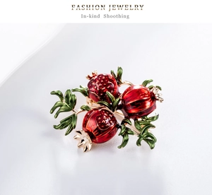 Detailed close-up of retro pomegranate brooch with red enamel seeds and green leaves