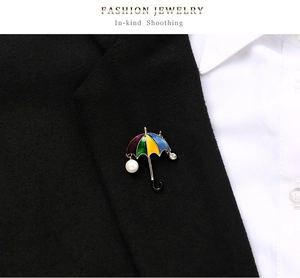 Detail of umbrella brooch with colorful enamel and pearl pinned on a black suit jacket