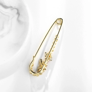 Spilla a balia dorata elegante con farfalla decorativa e perline su sfondo bianco puro