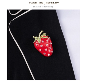 Détail d'une broche fraise en émail rouge et strass roses sur le revers d'un tailleur