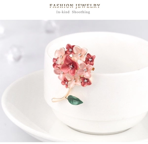Detail of flower brooch with pink enamel petals and pearls on a white ceramic cup
