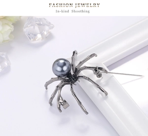 Detailed view of grey spider brooch with large pearl on a white frame background