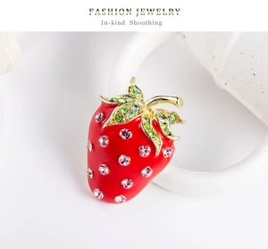 Détail d'une broche fraise en émail rouge avec strass brillants sur une tasse blanche