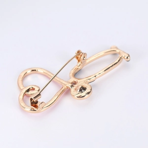 Close-up of golden stethoscope and heart shaped brooch with polished finish and safety pin