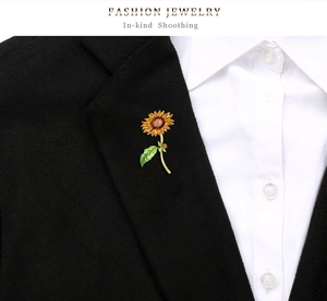 Detalle de broche de girasol artístico con esmalte prendido en la solapa de un blazer negro