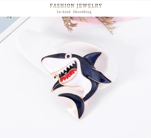 Detailed close-up of cartoon shark enamel brooch in blue and white with gold trim