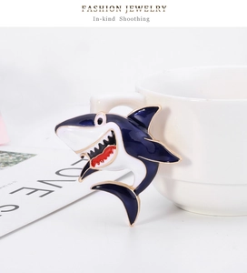 Close-up of a cartoon blue shark enamel brooch pinned to a white ceramic coffee cup