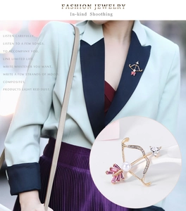 Detailed macro view of a gold-plated bow and arrow brooch with pink gems and pearls