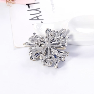 Back view of a vintage silver flower brooch with blue rhinestones on a white tray