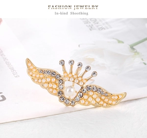 Détails d'une broche couronne ailes d'ange vintage avec strass brillants et perle
