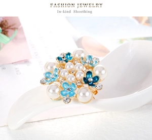 Detalle macro de broche de flor esmaltada azul con perlas y strass en aleación dorada