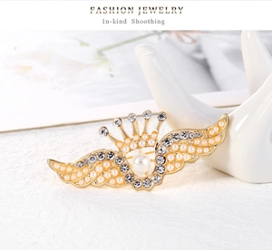 Détail d'une broche couronne ailée dorée avec perles et cristaux sur présentoir