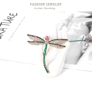 Detailed macro shot of a crystal dragonfly brooch on a white hand-shaped ceramic stand