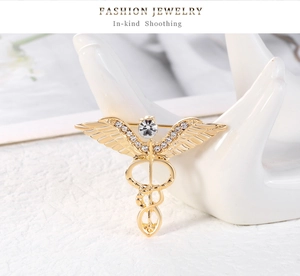 Macro shot of gold angel wing caduceus brooch with crystal rhinestones on a white stand
