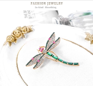 Detail of dragonfly brooch featuring emerald green crystals and gold metal plating