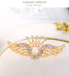 Vue détaillée d'une broche couronne ailée dorée avec perle centrale et cristaux de strass fins