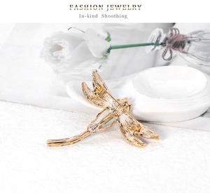 Detail view of gold dragonfly brooch back with secure pin clasp on a textured surface