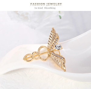 Macro shot of gold caduceus wing brooch with clear rhinestones on white display stand