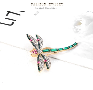 Detailed view of a gold-plated dragonfly brooch with green and white crystals