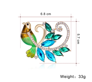 Vue détaillée d'une broche phénix dorée avec cristaux verts et dimensions 6,8x5,7 cm