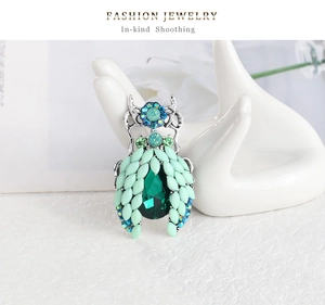 Macro shot of beetle brooch with emerald center and green marquise stones on a hand stand