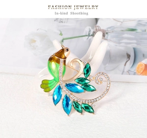 Détail d'une broche phénix dorée sertie de cristaux verts sur un modèle de main blanche