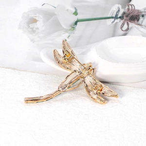 Back view of gold dragonfly brooch showing safety pin clasp on white textured surface