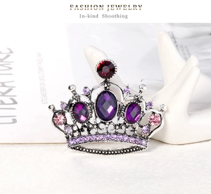 Macro detail of crown brooch featuring purple oval stones and crystals on a white prop