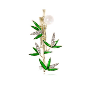 Detail view of a gold bamboo brooch with green enamel leaves, crystals, and a pearl