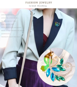 Détail d'une élégante broche phénix verte avec cristaux sur revers de veste pastel