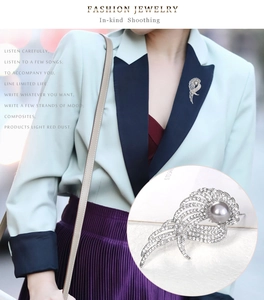Détail d'une broche aile argentée avec perle grise et strass portée sur une veste chic