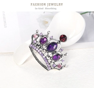 Close-up of royal crown brooch with purple rhinestones on a polished silver frame