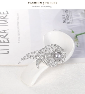 Détail d'une broche aile en argent avec perle grise et strass brillants sur céramique