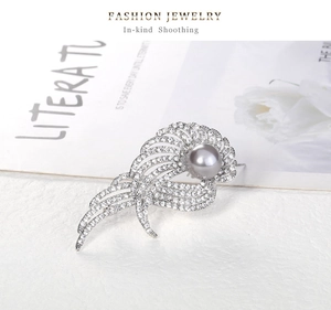 Détail d'une broche aile en argent avec perle grise et strass brillants sur un magazine