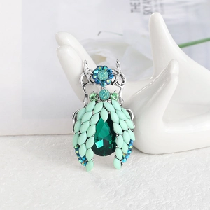 Elegant beetle insect brooch with emerald rhinestones displayed on a white hand stand