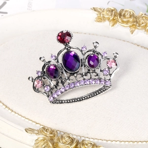 Vintage silver crown brooch with purple rhinestones on a white textured fabric background