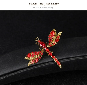 Detail of dragonfly brooch with red rhinestones and golden wings on a black surface