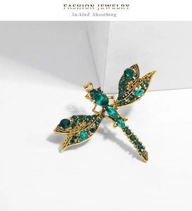 Macro detail of vintage gold dragonfly brooch with green rhinestones on white stones