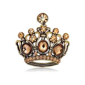 Broche couronne vintage en or avec cristaux ambrés et strass sur fond blanc épuré
