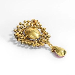 Broche vintage en cristal doré avec pendentif goutte et strass rouges sur fond blanc