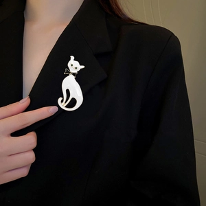 Broche chat en émail blanc avec yeux verts fixée sur le revers d'un costume