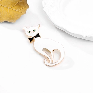 Détail d'une broche chat en émail blanc avec nœud noir et yeux en pierres précieuses vertes